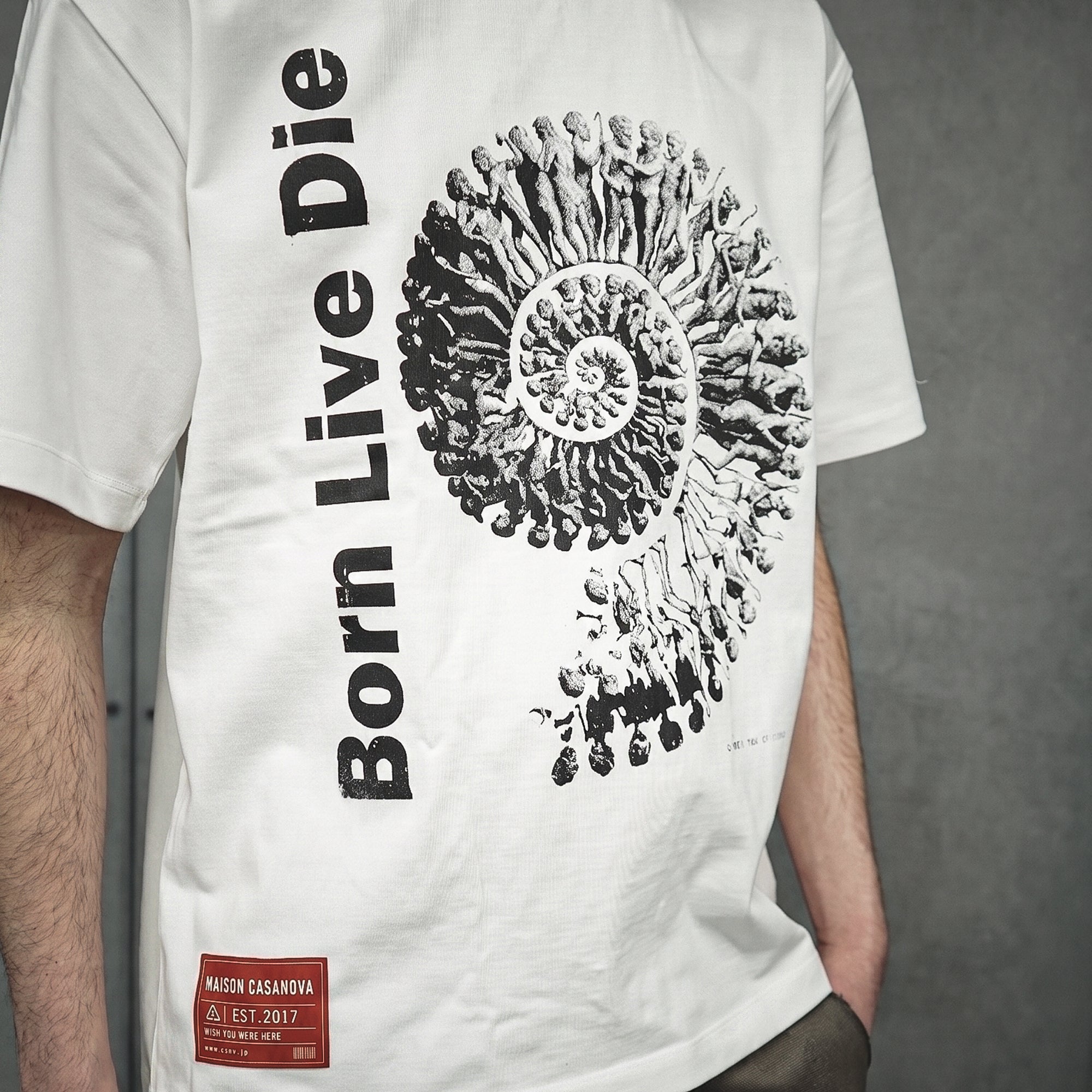 メゾンカサノバ 白のグラフィックTシャツ。フロントに縦書きで「Born Live Die」の文字と、人が渦を巻くようなモノクロイラスト。左裾に赤いブランドラベル付き。