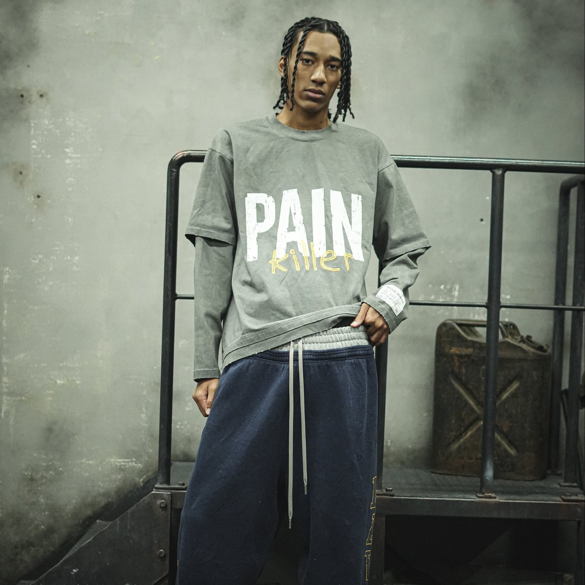 Maison Casanovaのヴィンテージ加工されたダークグレーのレイヤード長袖Tシャツ。前面に白いかすれプリントで「PAIN」、その下に黄色の立体刺繍で「killer」のロゴデザイン。左袖口に白いブランドタグ付き。