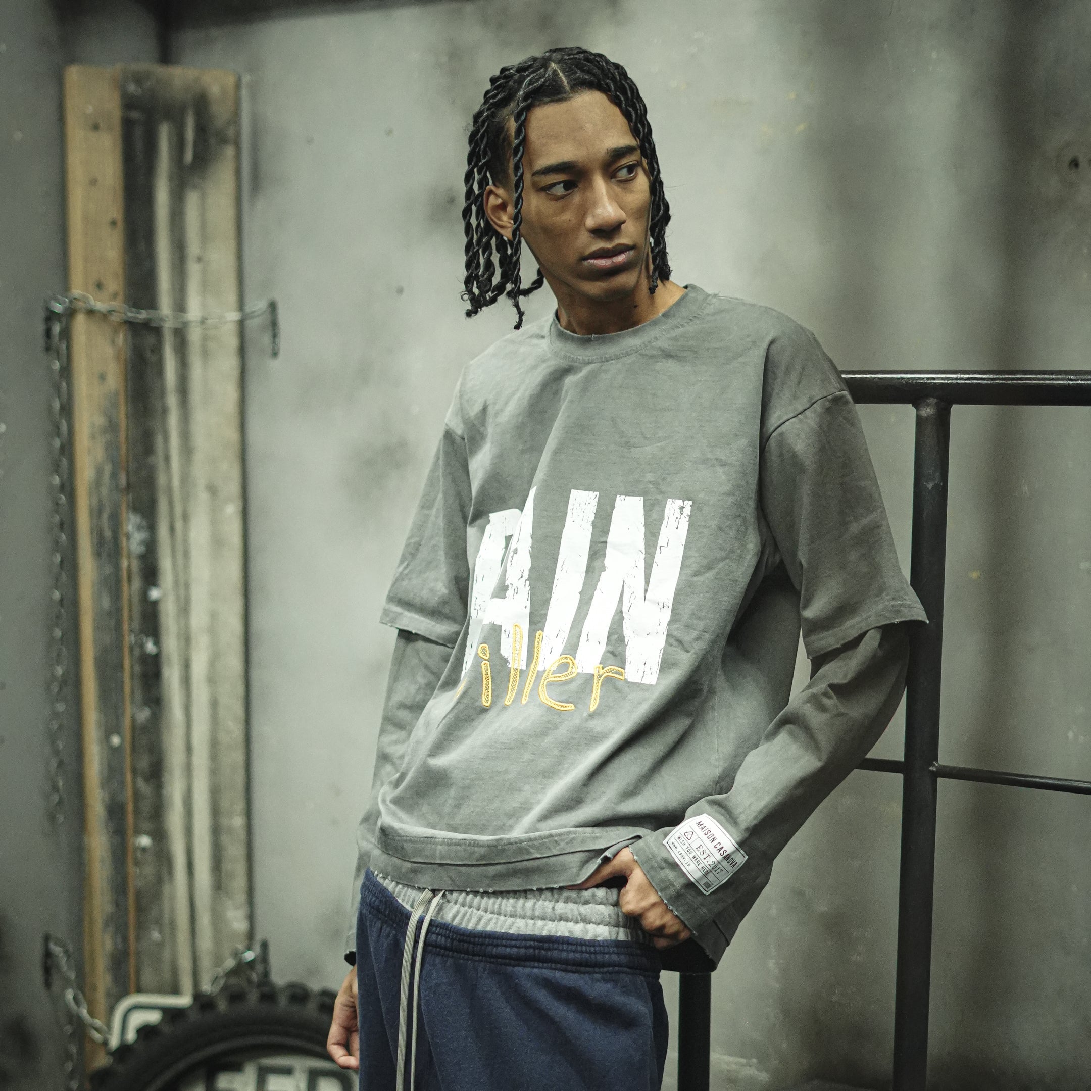 Maison Casanovaのヴィンテージ加工されたダークグレーのレイヤード長袖Tシャツ。前面に白いかすれプリントで「PAIN」、その下に黄色の立体刺繍で「killer」のロゴデザイン。左袖口に白いブランドタグ付き。