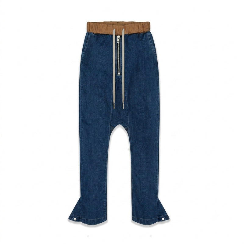 MAISON CASANOVAのブルーデニムのドロップクロッチパンツ。ウエスト部分はブラウンの異素材で切り替えられている。フロントには長いドローストリングと目立つシルバーのジップ。裾の両サイドにはシルエット調整用のスナップボタンが配置されている。