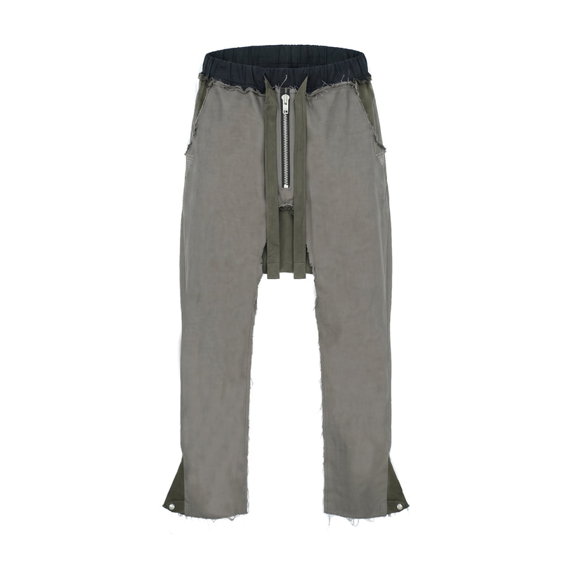 MAISON CASANOVAのオリーブグレー（カーキ系）のドロップクロッチパンツ。上部の黒いウエストバンドの下は切りっぱなしのフリンジ状になっている。フロント中央にはシルバーのジップがあり、その両サイドから太くて長い布製の紐が垂れ下がっている。脚の内側などにダメージ加工があり、裾の両サイドにはシルエット調整用のスナップボタンが付いている。